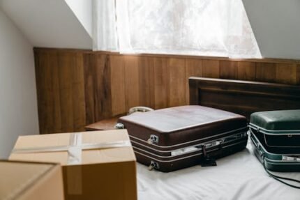 From above of brown and green vintage suitcases and packed carton boxes placed on bed with sheet in light room with sloping roof